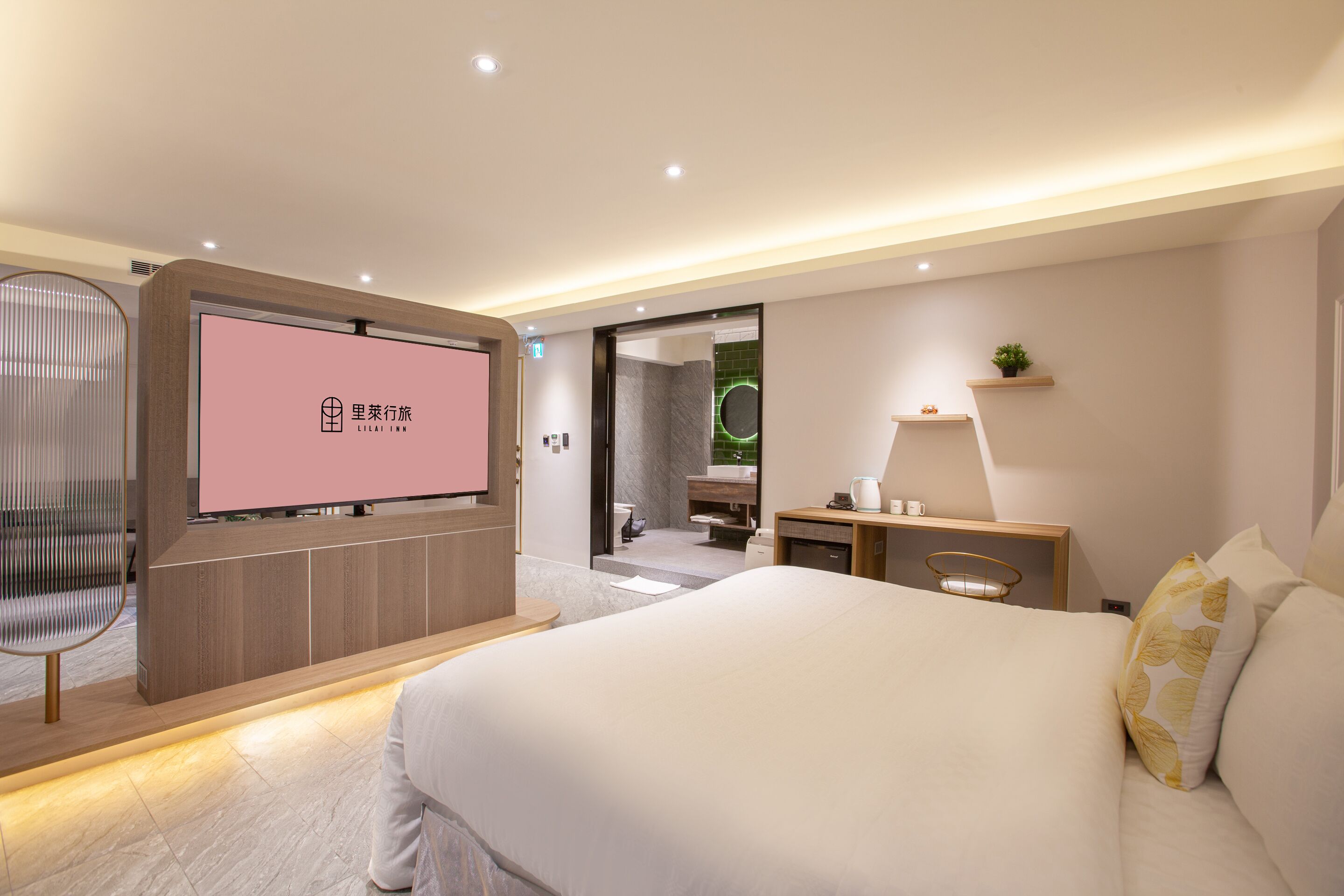 A modern hotel room with a large bed, a television, a desk, and a bathroom visible through an open door.