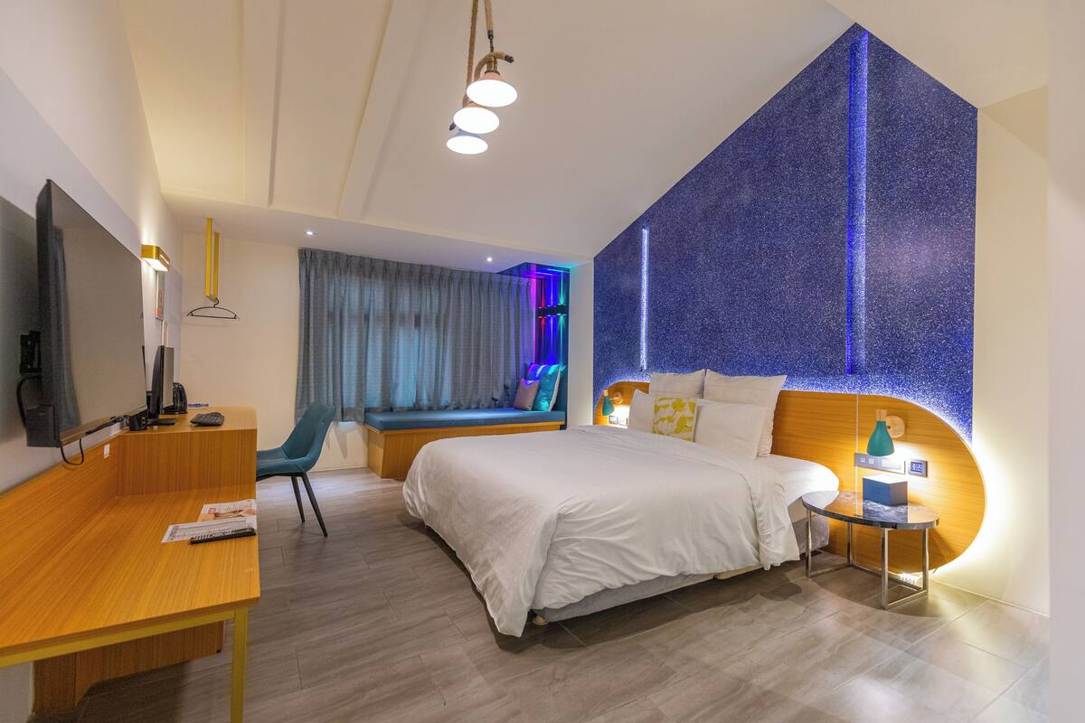Une chambre d’hôtel moderne dotée d’un grand lit, d’un bureau, d’un coin salon et d’un mur agrémenté d’un élément d’éclairage original.