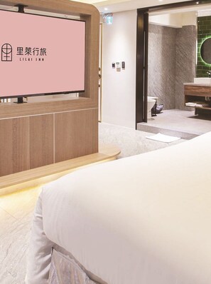 Een hotelkamer met een bed, een tv die aan een houten paneel bevestigd is, en een badkamer die zichtbaar is door een geopende deur.