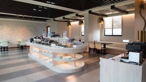 Un comedor moderno con una estación de buffet central, mesas dispuestas y un amplio ventanal que proporciona luz natural.