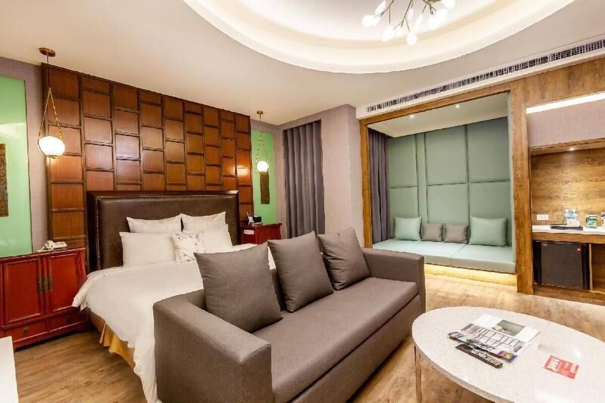 A hotel room with a bed, a sofa, a small table, a mirror, and a wooden panel wall.
