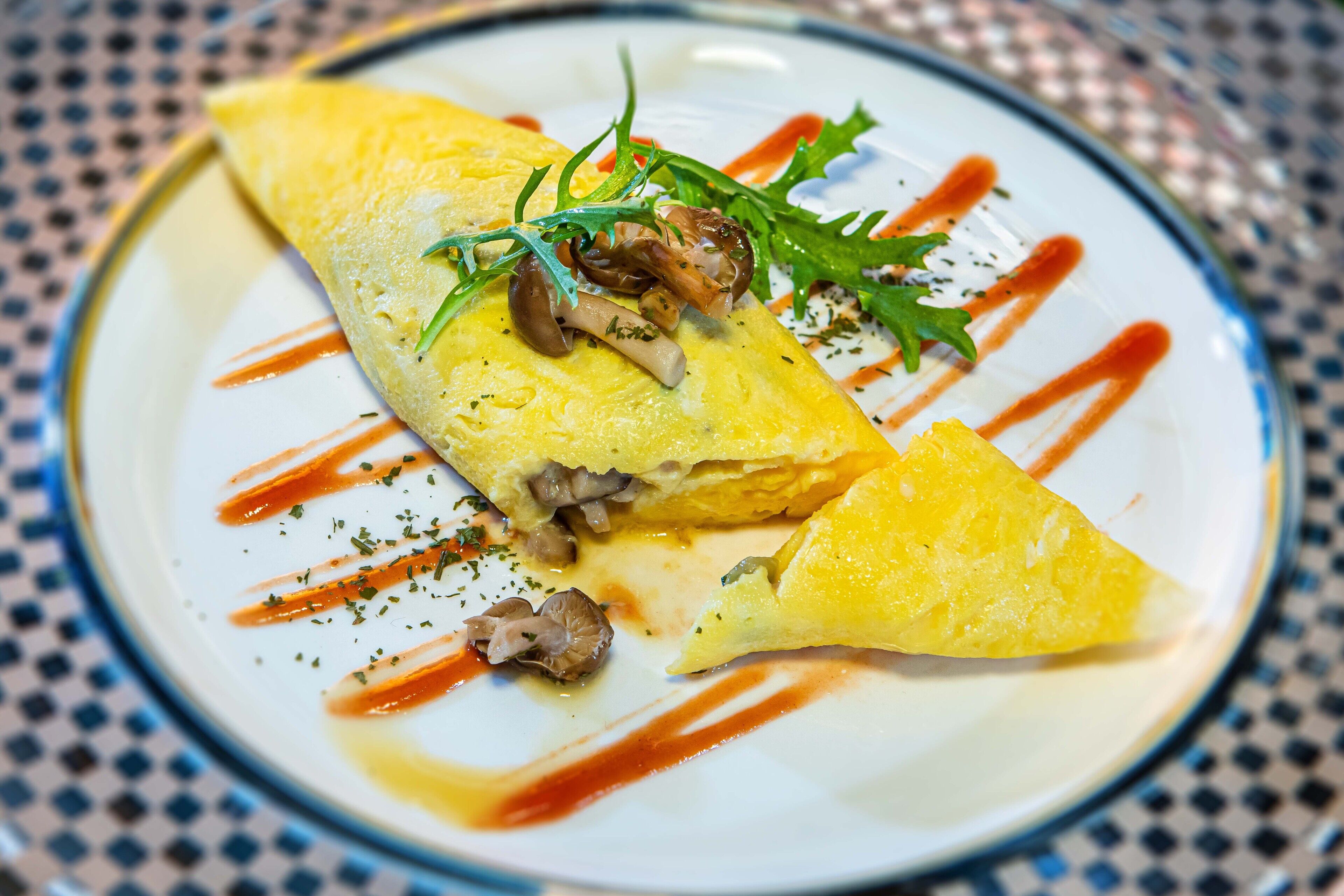A plate with an omelette, mushrooms, and greens, served on a patterned tablecloth.