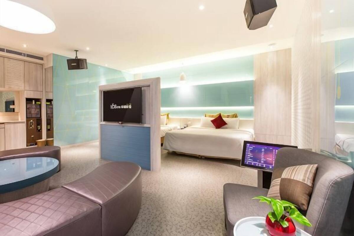 A modern hotel room with a bed, a TV, a seating area, and a small table with a plant.