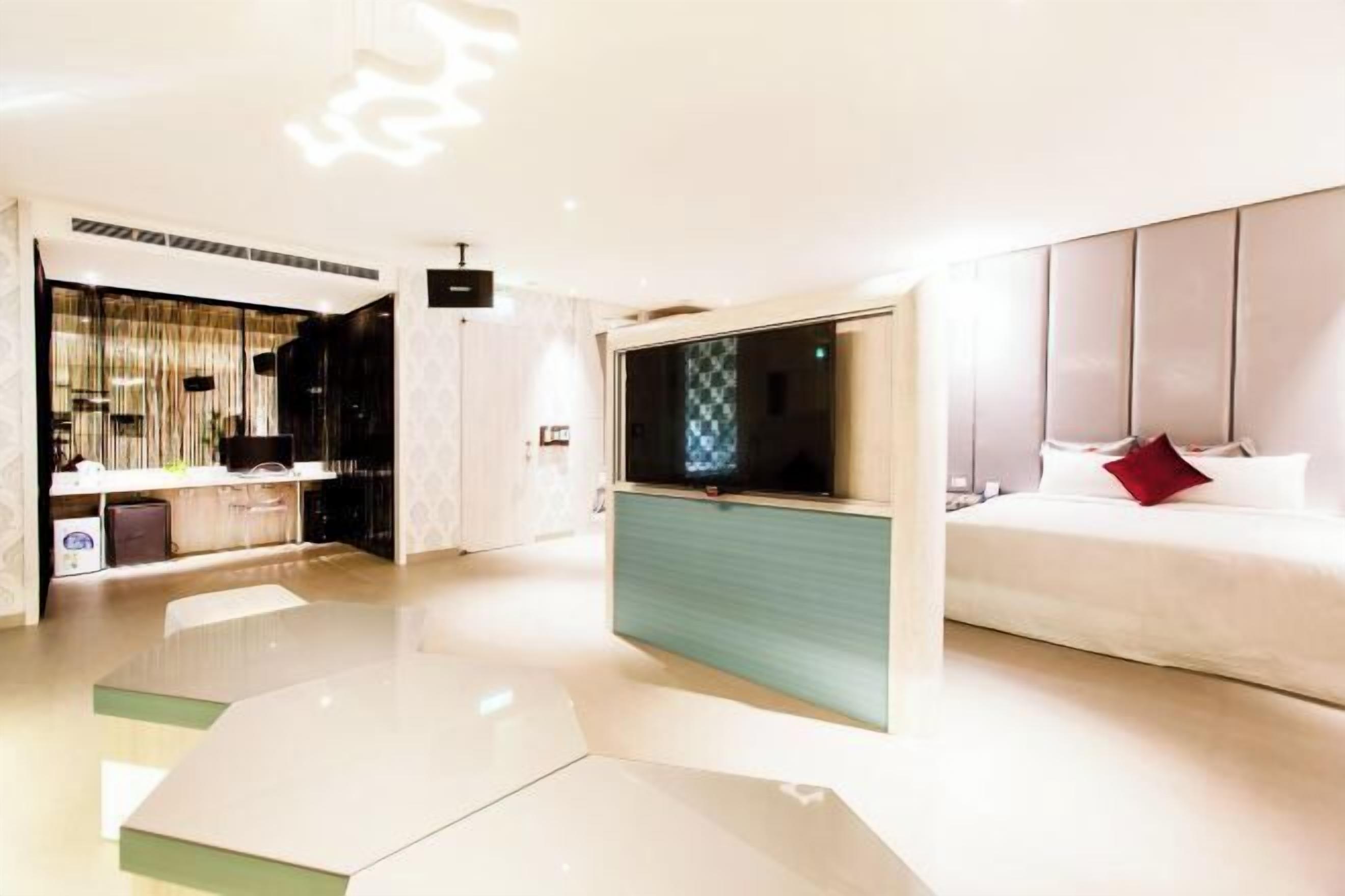 A modern hotel room with a bed, a TV, a desk, and a seating area.