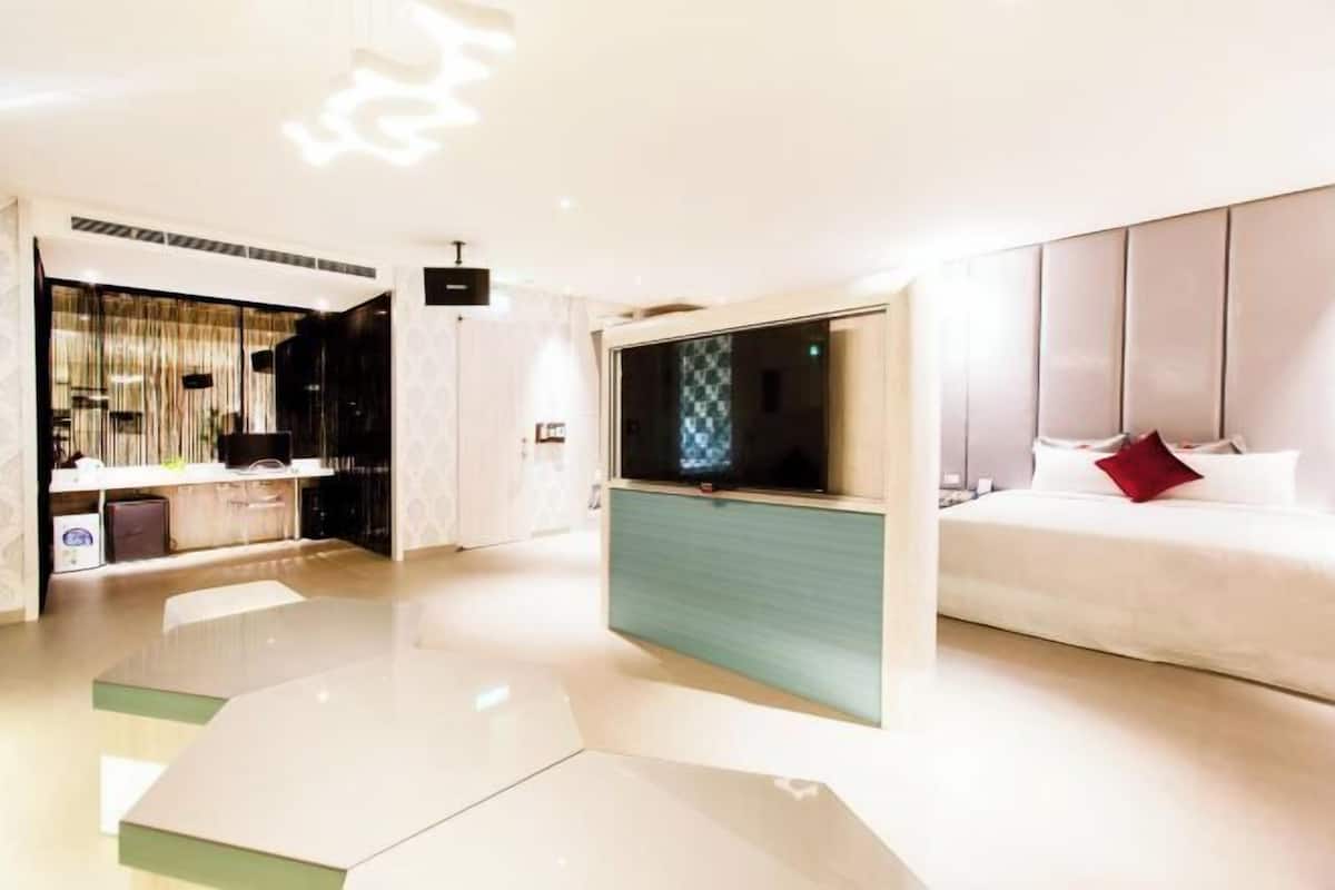 A modern hotel room with a bed, a TV, a desk, and a seating area.