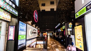 Un couloir doté d’un sol à carreaux, de panneaux publicitaires numériques et d’une enseigne iHotel bien visible.