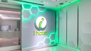 Un espace d’accueil moderne, avec un logo « i hotel » bien visible, un design épuré et un éclairage néon vert qui apporte une touche d’originalité.