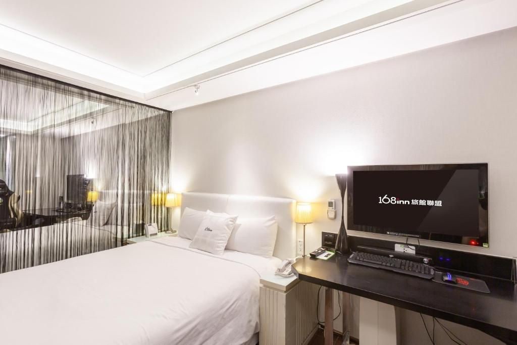 A hotel room with a bed, a desk with a computer, a television, and a mirror.