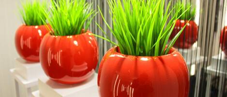 Tres plantas rojas en macetas con césped verde sobre pedestales blancos.