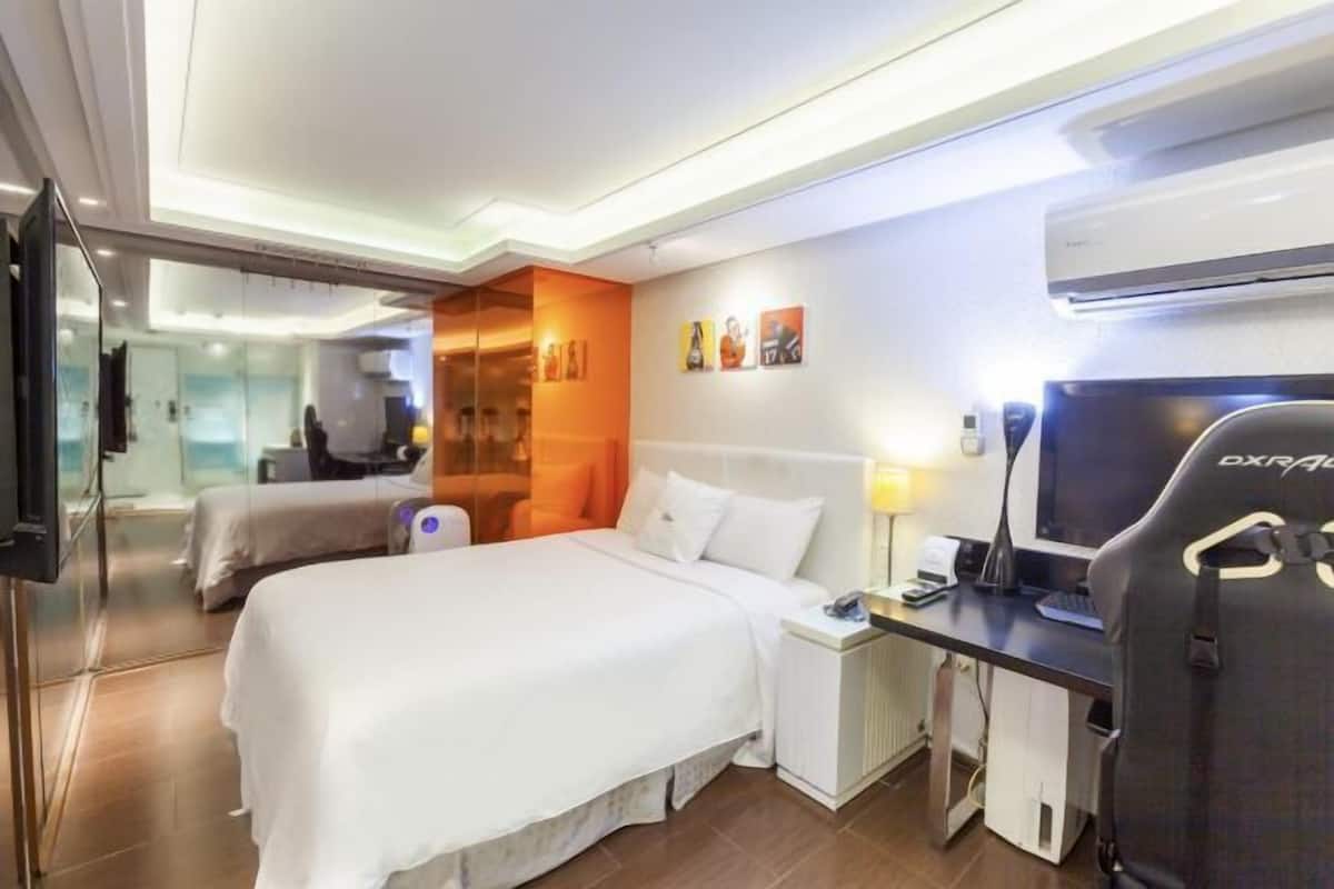 Una habitación de hotel con cama, escritorio, silla, televisor y aire acondicionado.