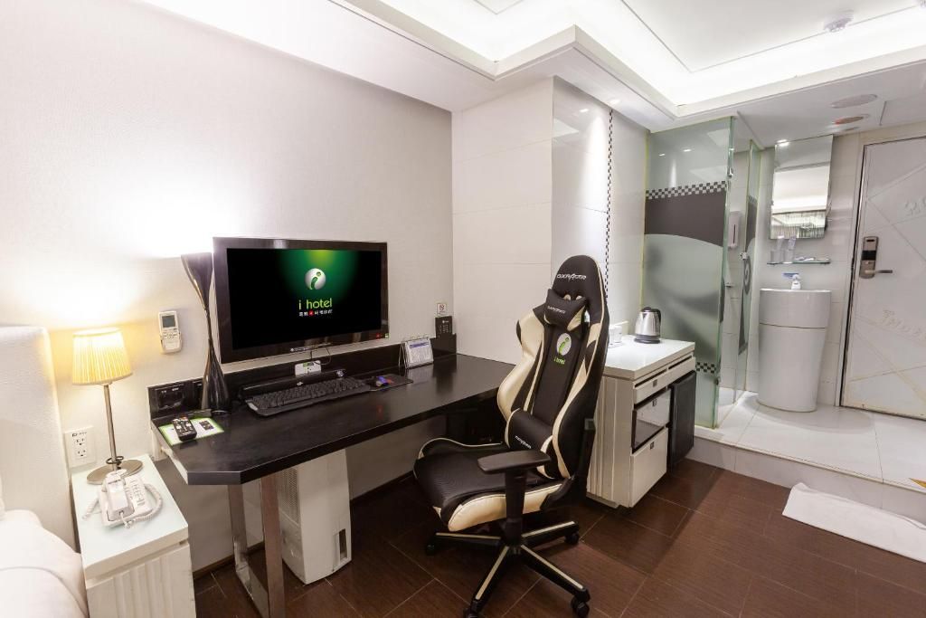 A hotel room with a desk, computer, chair, and a shower area.
