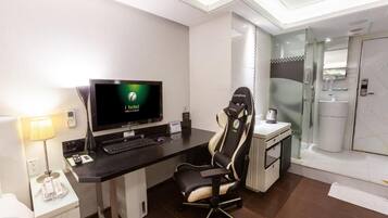 Habitación de hotel con escritorio, computadora, silla y zona de ducha.