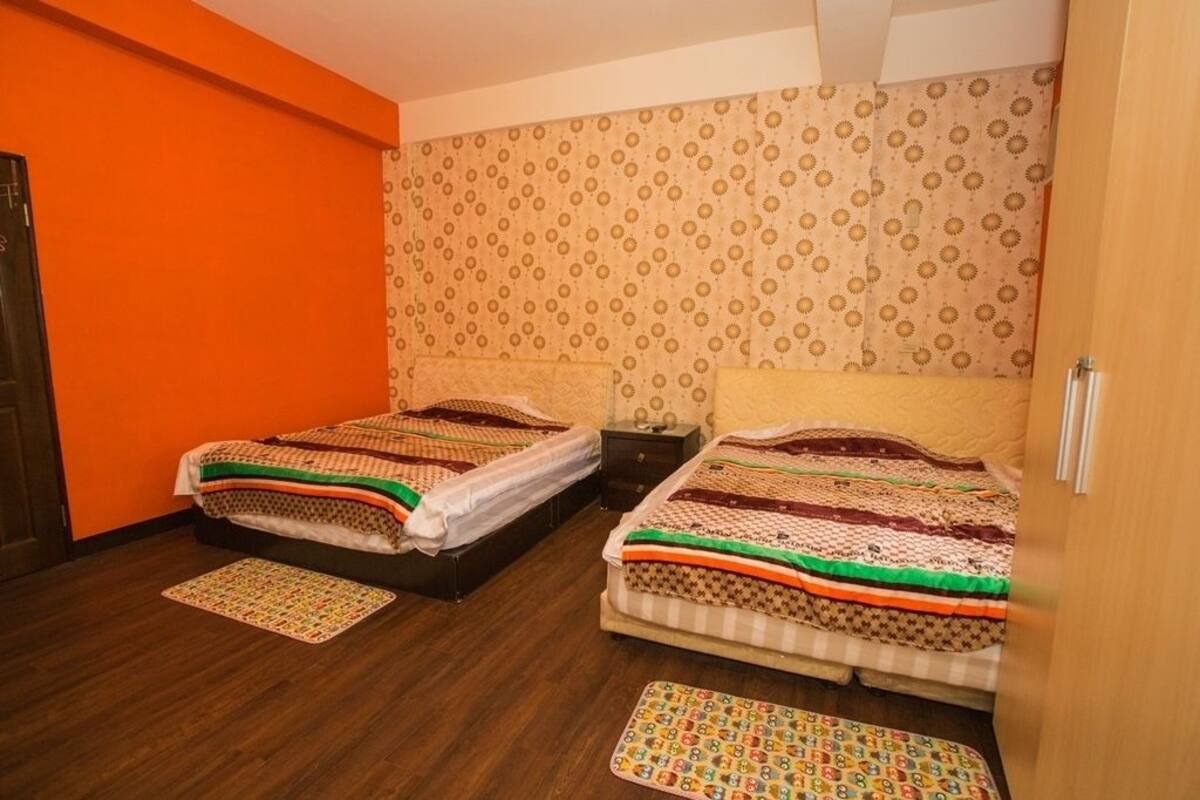 A room with two beds, a wooden floor, and patterned wallpaper.