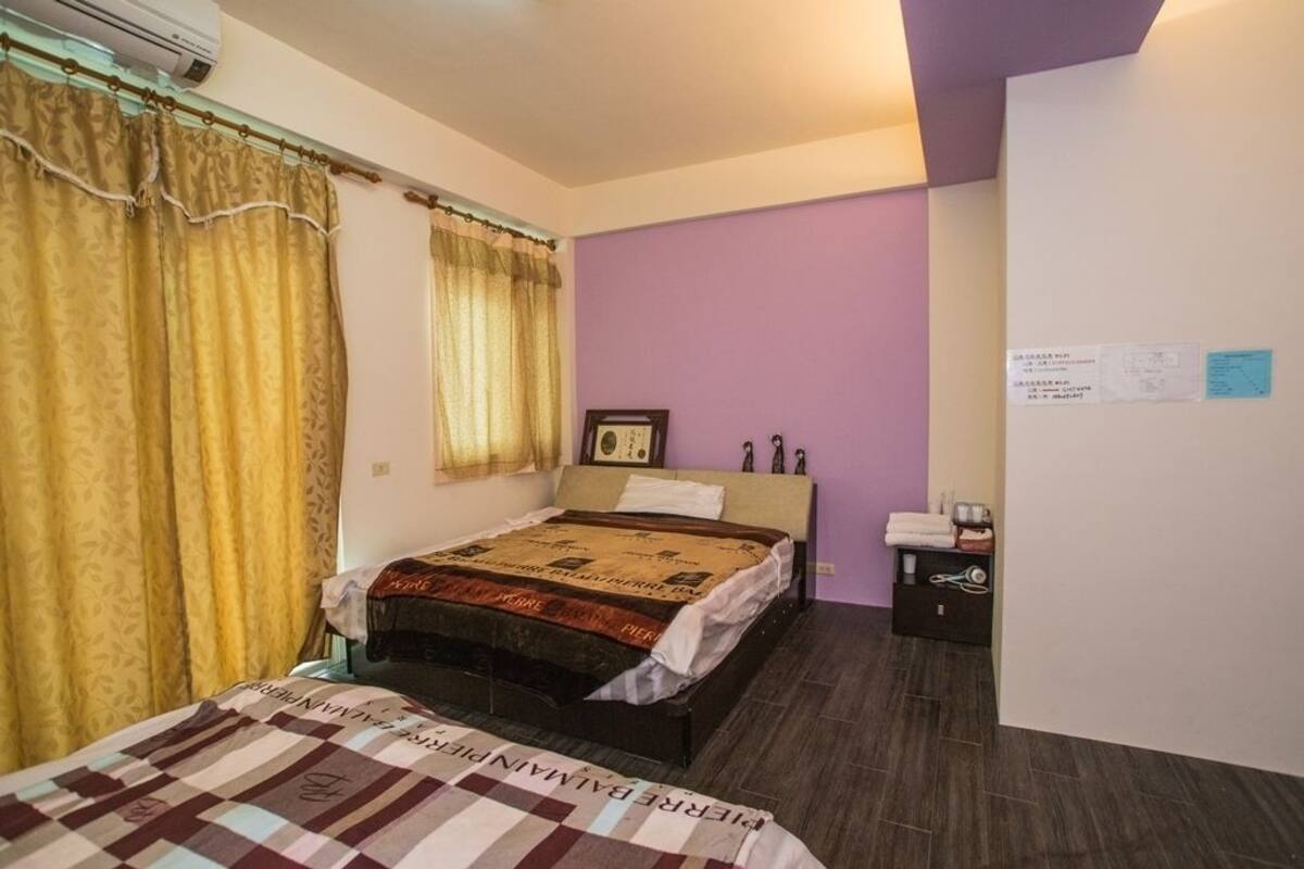 A bedroom with a bed, a nightstand, a wall-mounted air conditioner, and a purple accent wall.