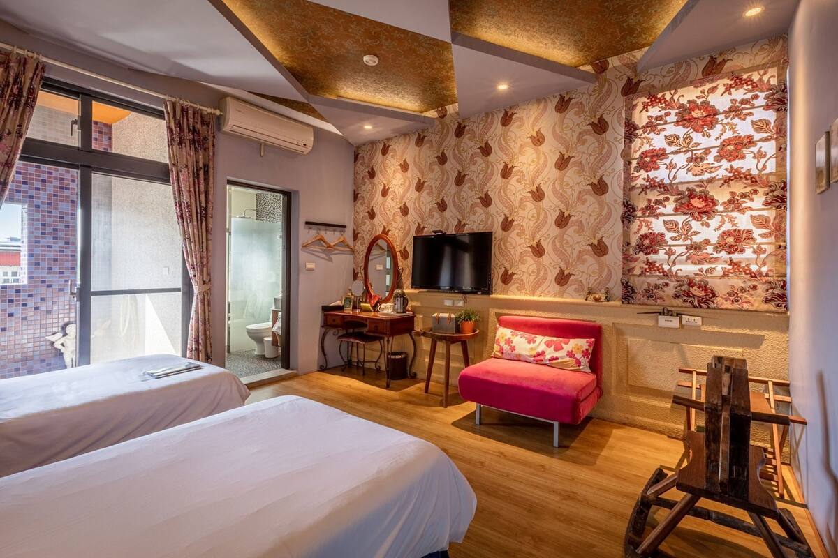 A hotel room with two beds, a desk, a television, and a red chair.