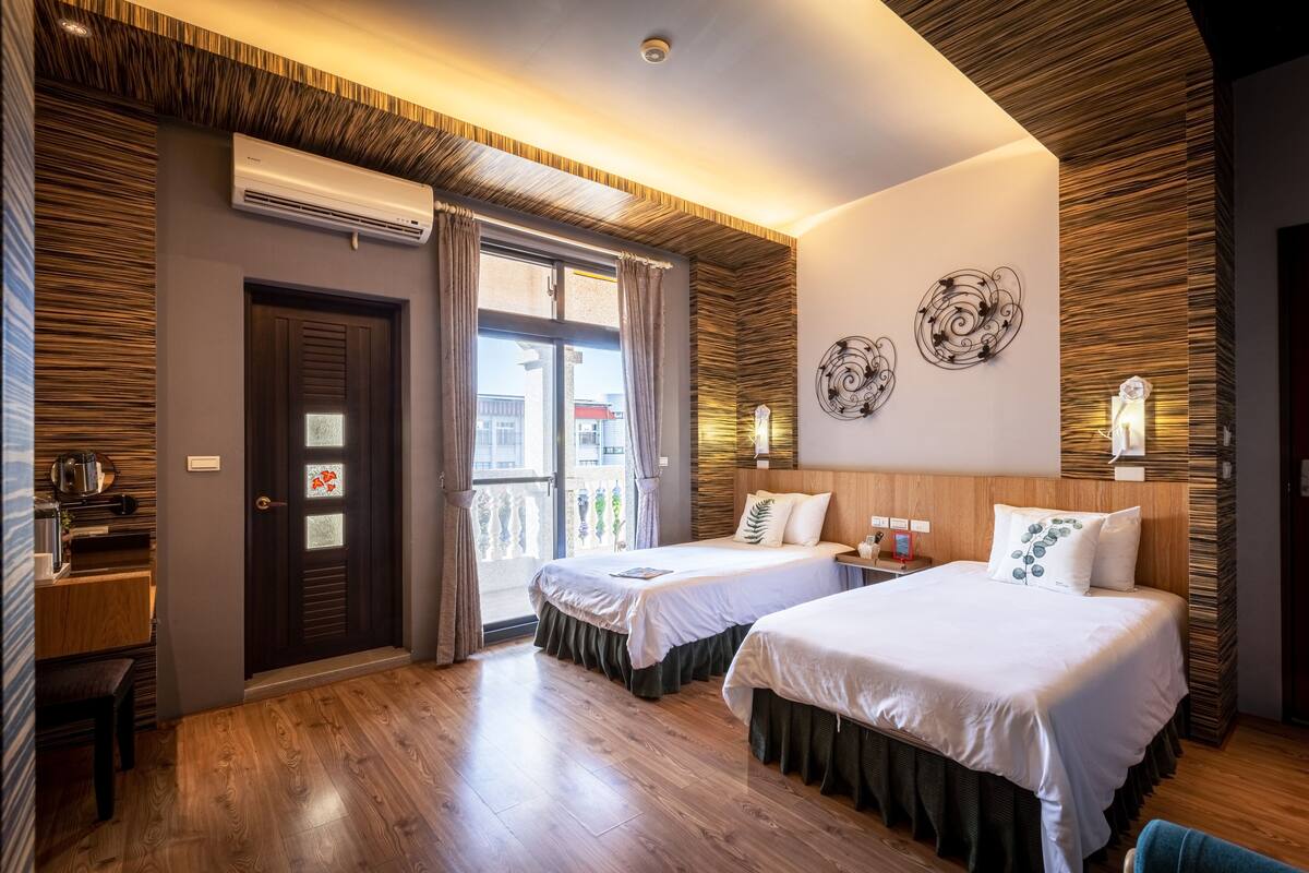A hotel room with two beds, a wooden ceiling, a balcony, and a small kitchenette.