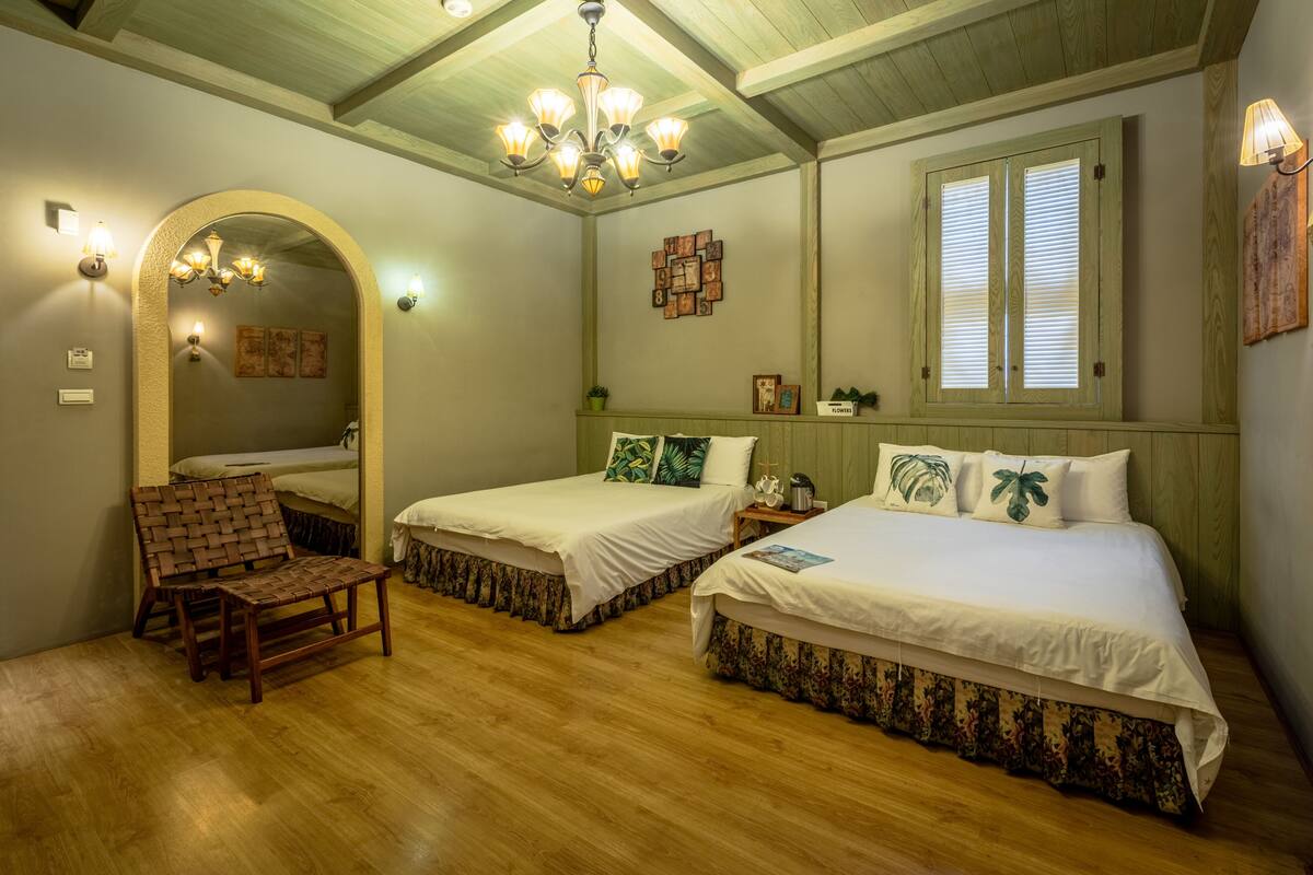 A room with two beds, a wooden chair, a chandelier, and a mirror.