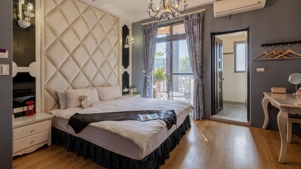 A bedroom with a tufted headboard, a chandelier, a bedside table with a lamp, and a view through a glass door. - Queen Love (Hualien City)