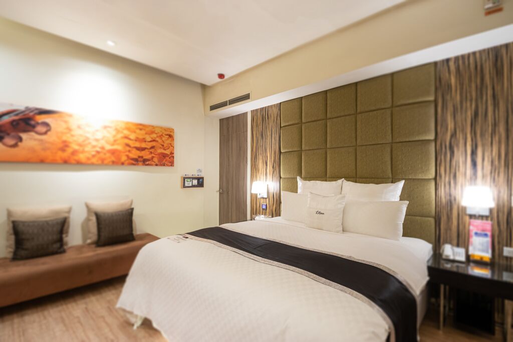 A hotel room with a large bed, a sofa, a wall-mounted artwork, and a bedside table.