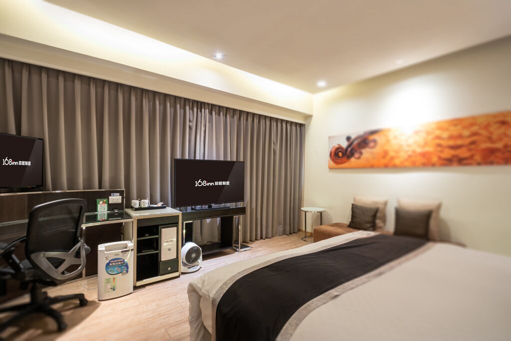 A hotel room with a bed, desk, chair, television, and a wall-mounted artwork.