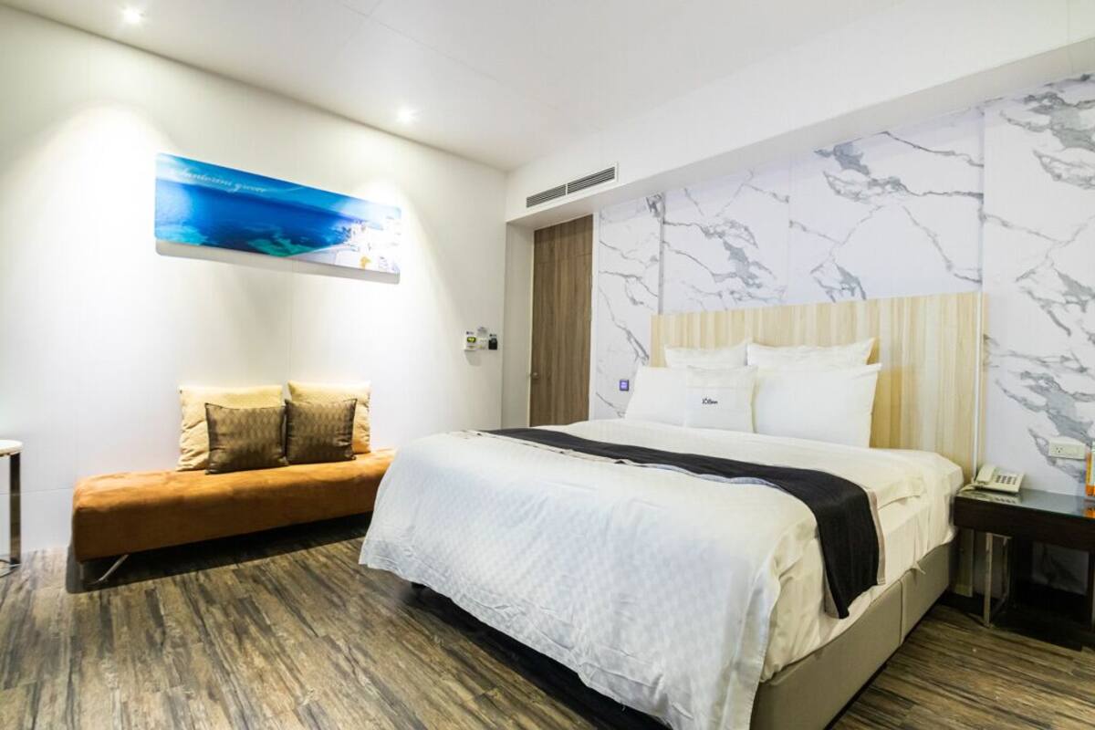 Een moderne hotelkamer met een groot bed, een bank, een wand met marmerpatroon en een schilderij van een zeegezicht.