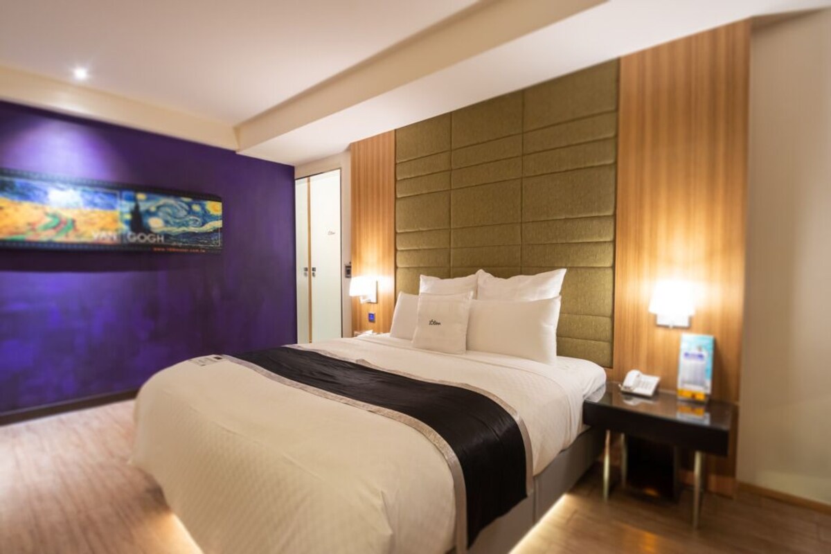 Une chambre d’hôtel avec un lit, des tables de chevet, un tableau au mur et une porte.