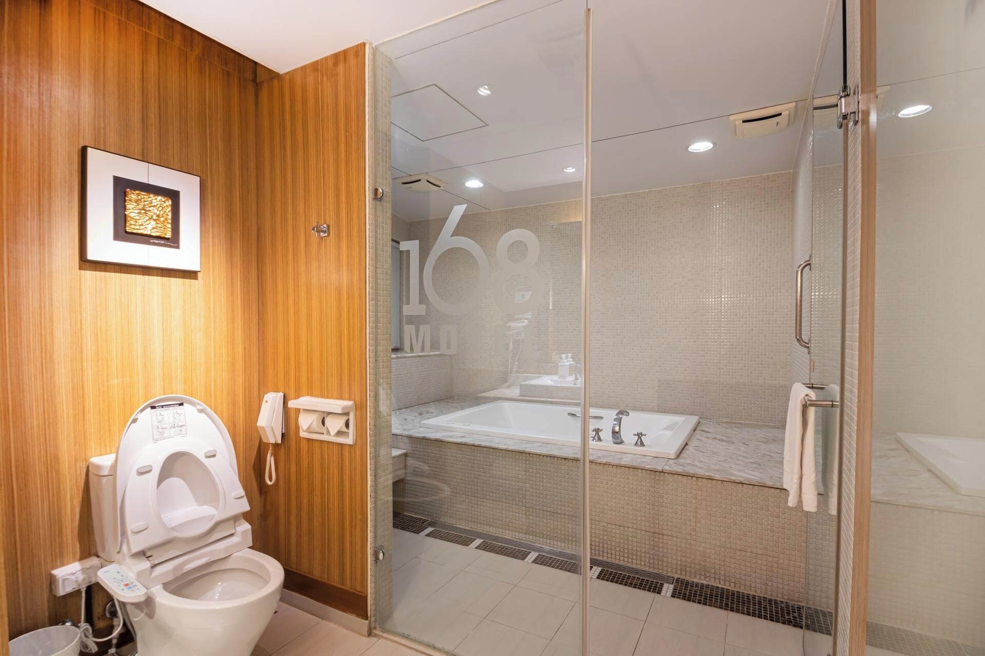 A modern bathroom with a wooden panel wall, a glass-enclosed shower, a white toilet with a bidet, and a large mirror.