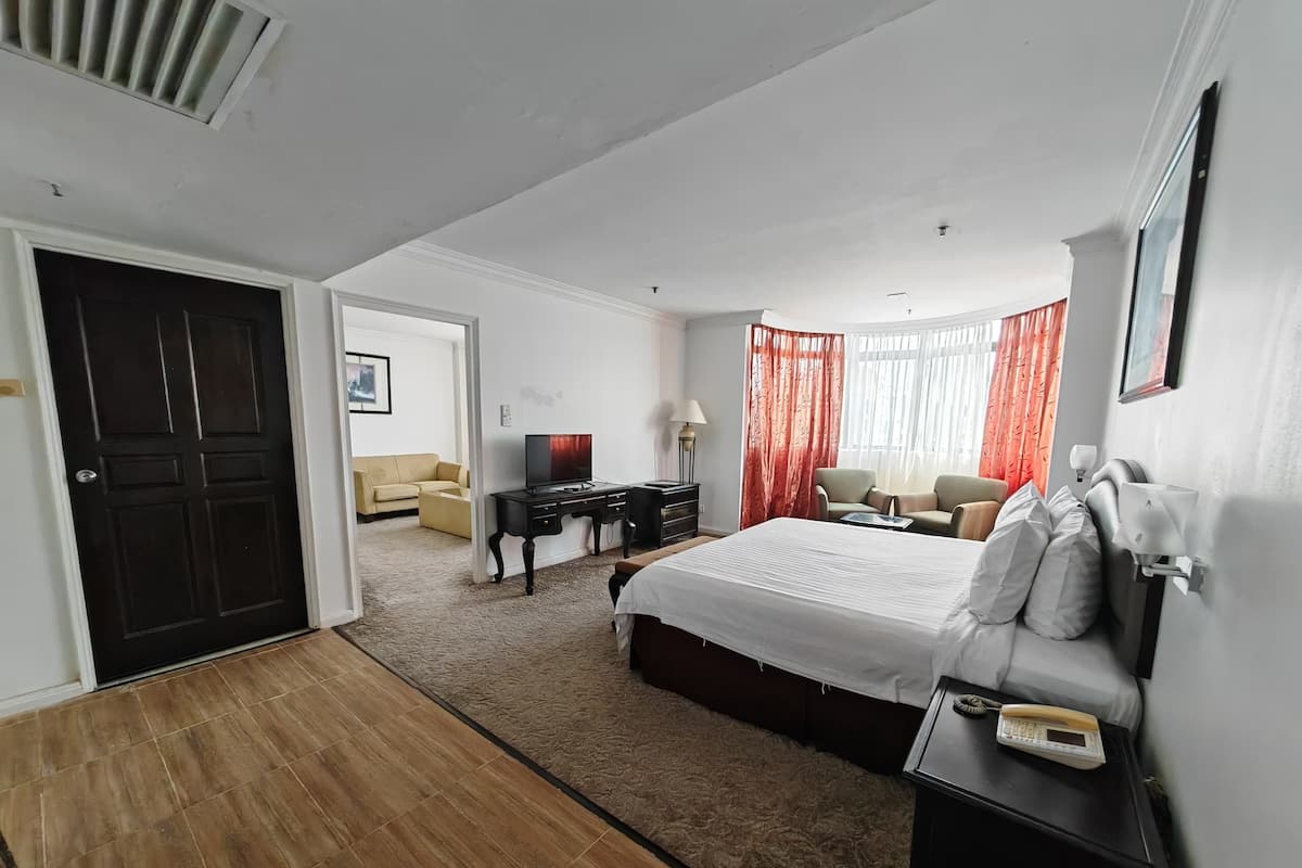 A hotel room with a large bed, a desk with a computer, a chair, a sofa, and a TV.