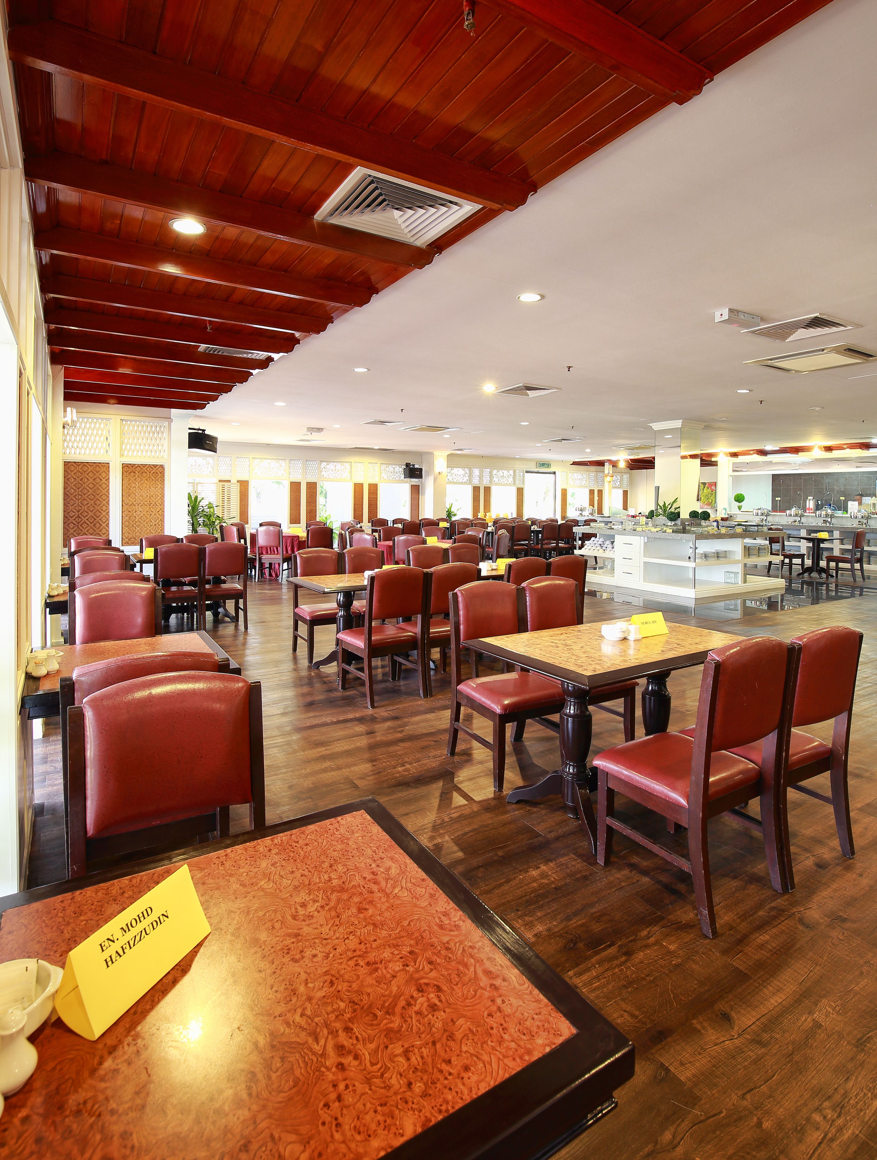 A spacious restaurant with wooden flooring, red upholstered chairs, and tables with yellow name cards.
