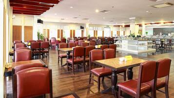 A spacious restaurant with wooden flooring, red upholstered chairs, and tables with yellow name cards.
