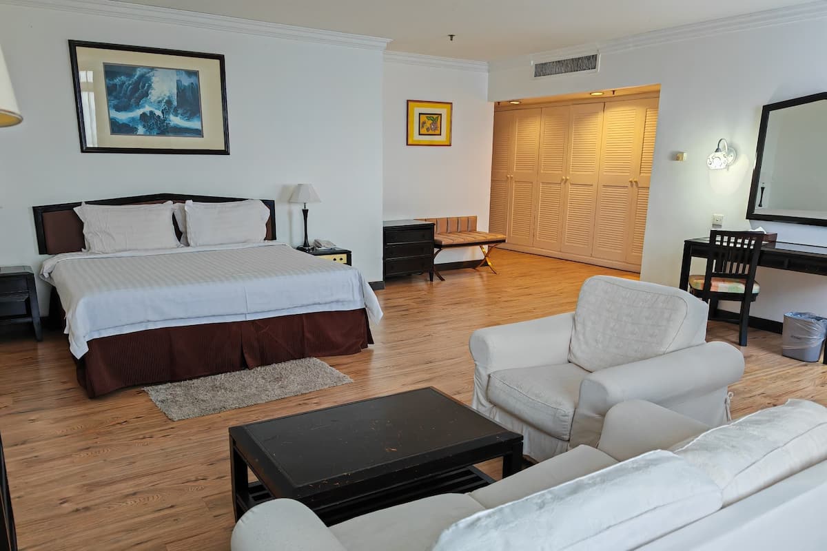 A well-lit bedroom with a large bed, bedside tables, a desk, and a chair. There is a wardrobe with sliding doors and a mirror.