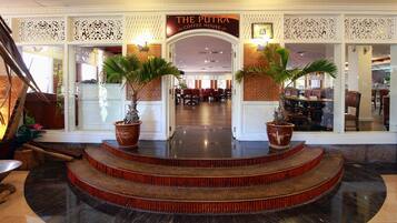 Entrada de un hotel con un letrero que dice "The Putra Coffee House", destacando una escalera con plantas en macetas y una pared decorativa.