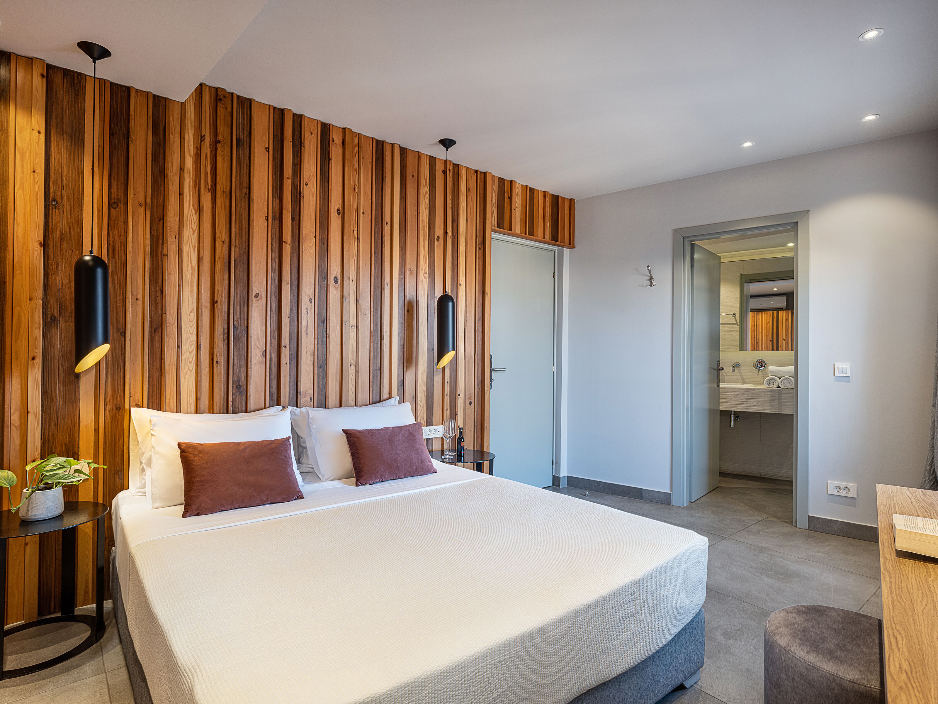 Een moderne slaapkamer met een groot bed, een wand van houten panelen, twee bedlampjes en een badkamer zichtbaar door een open deur.