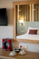 A hotel room with a bed, a bedside table with a coffee maker, cups, and a mirror reflecting the room.