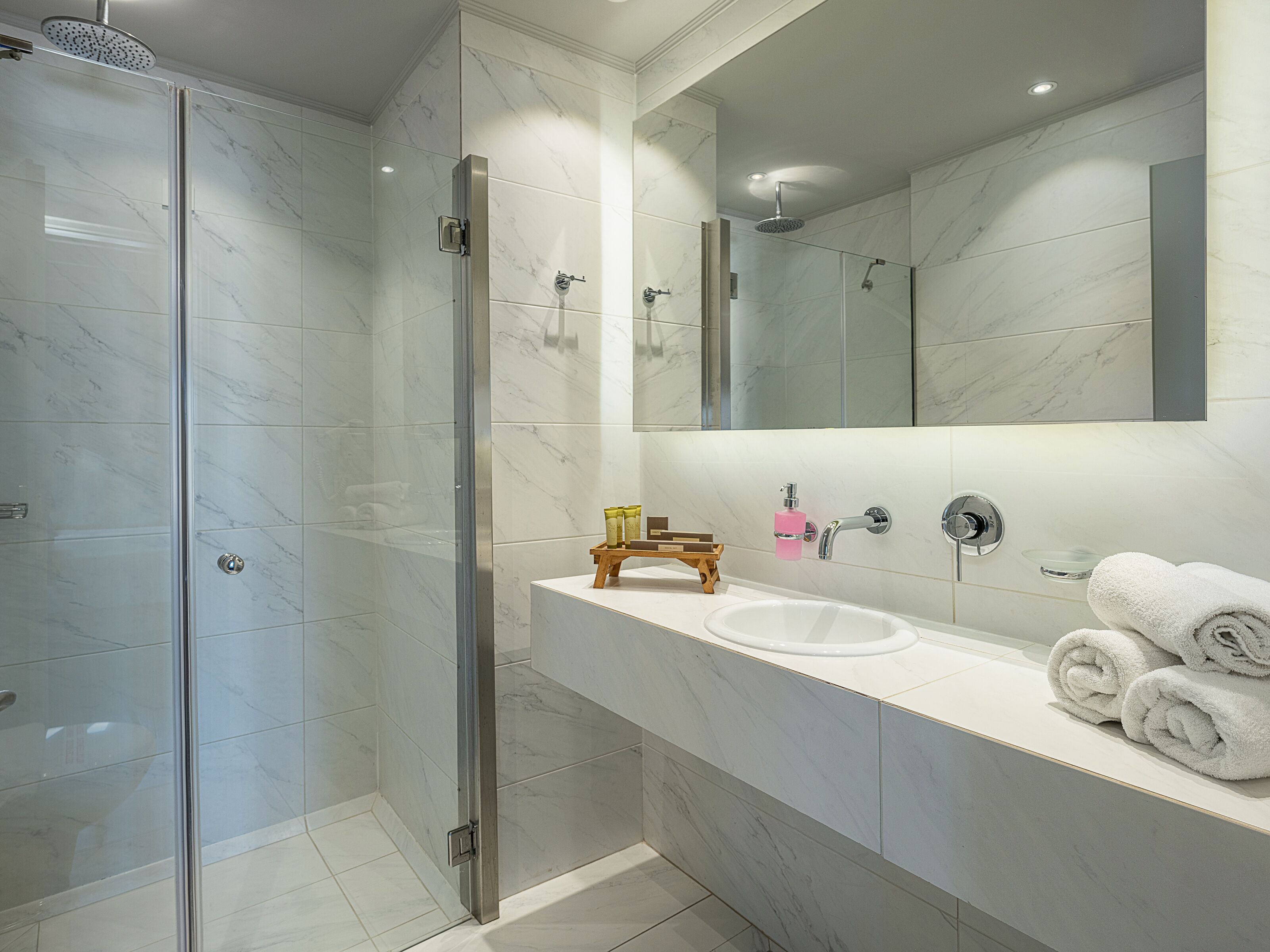 Un baño moderno con ducha acristalada, lavamanos blanco y espejo sobre él.