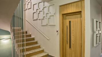 Una escalera con barandilla, una puerta de madera e interruptores de luz fijados a la pared.