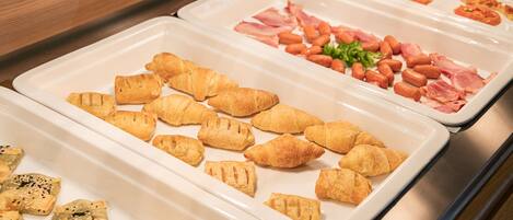 A buffet with various food items including croissants, ham, and beans.
