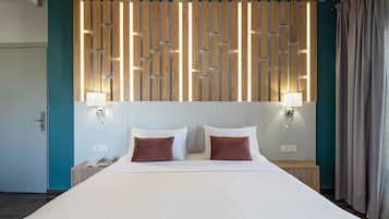 Een hotelkamer met een groot bed, een houten hoofdeinde, twee bedlampen en een wand in teal blauw.