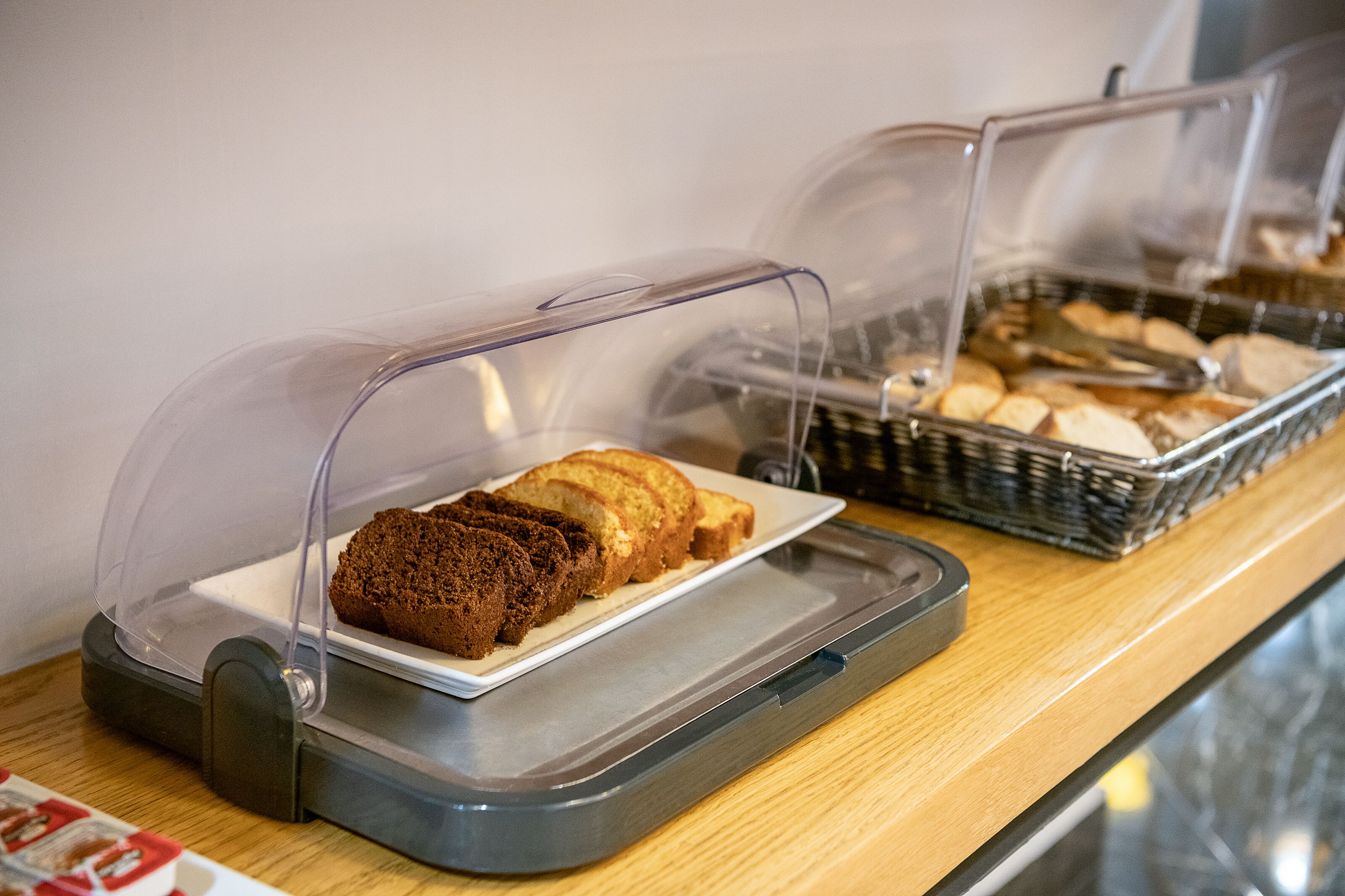 A buffet counter with bread and pastries under protective covers.