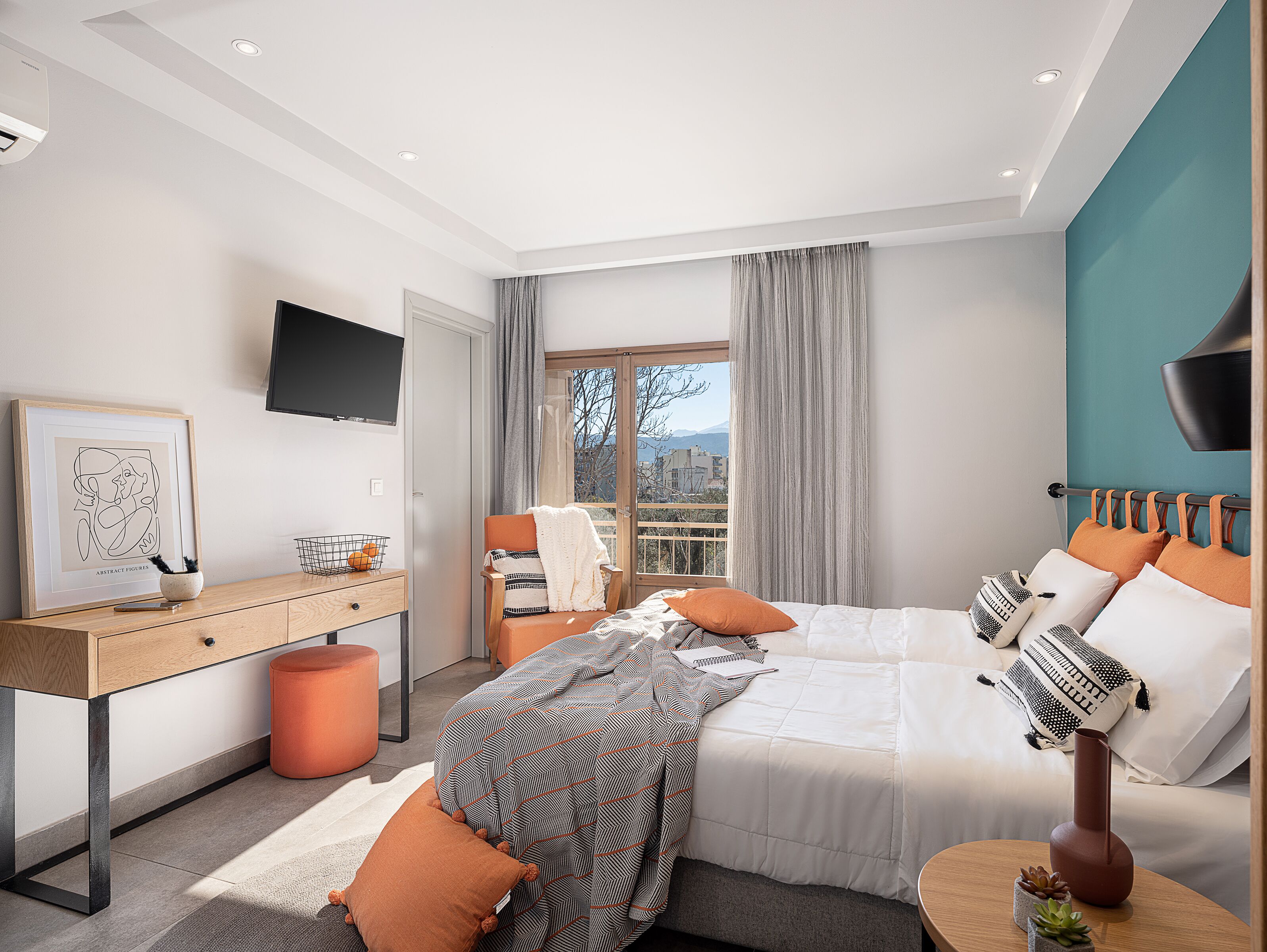 A modern bedroom with a bed, desk, and a view of the outdoors.