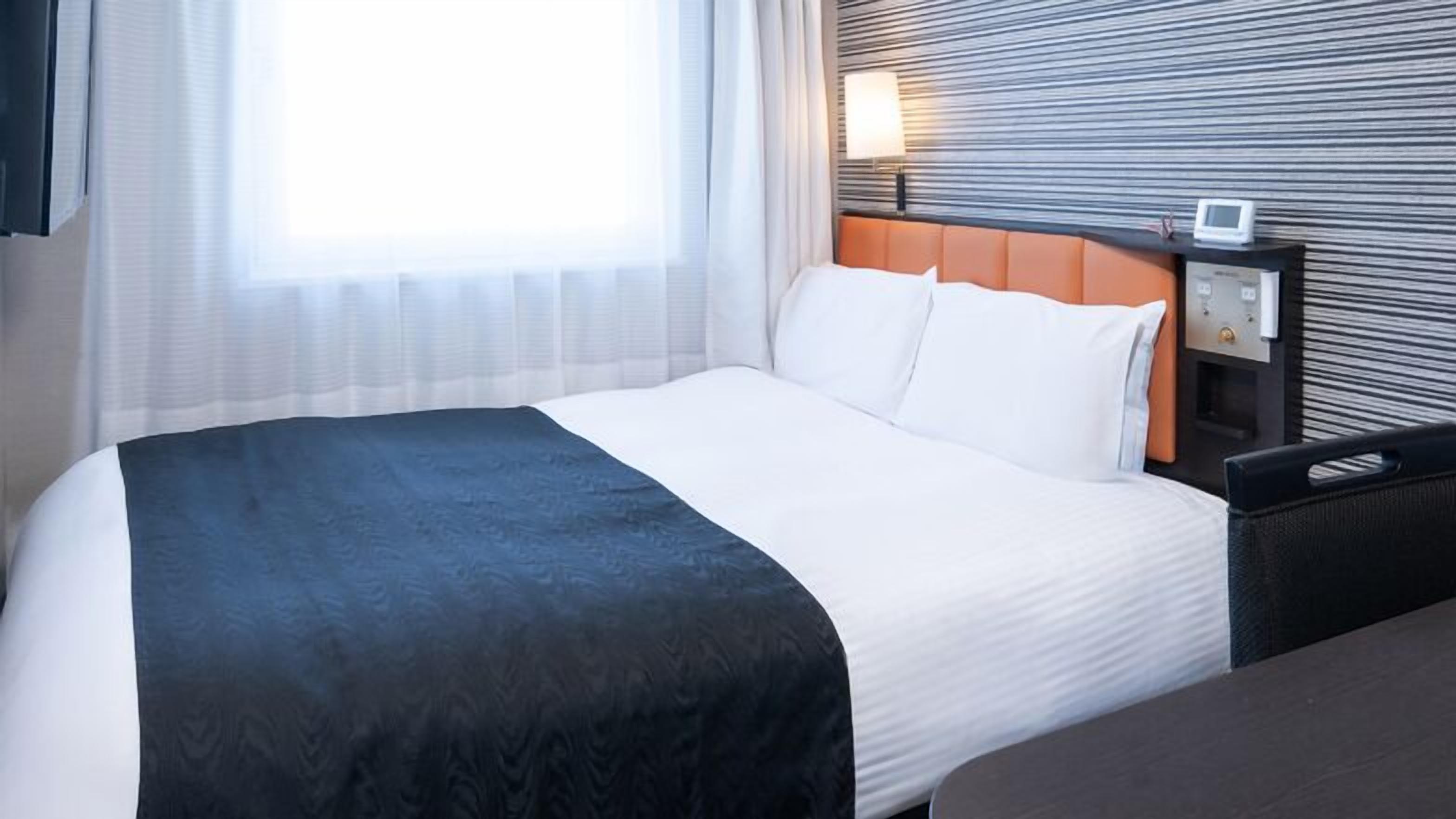 Hotelkamer met een groot bed, nachtkastje met lamp en uitzicht buiten door dunne gordijnen.
