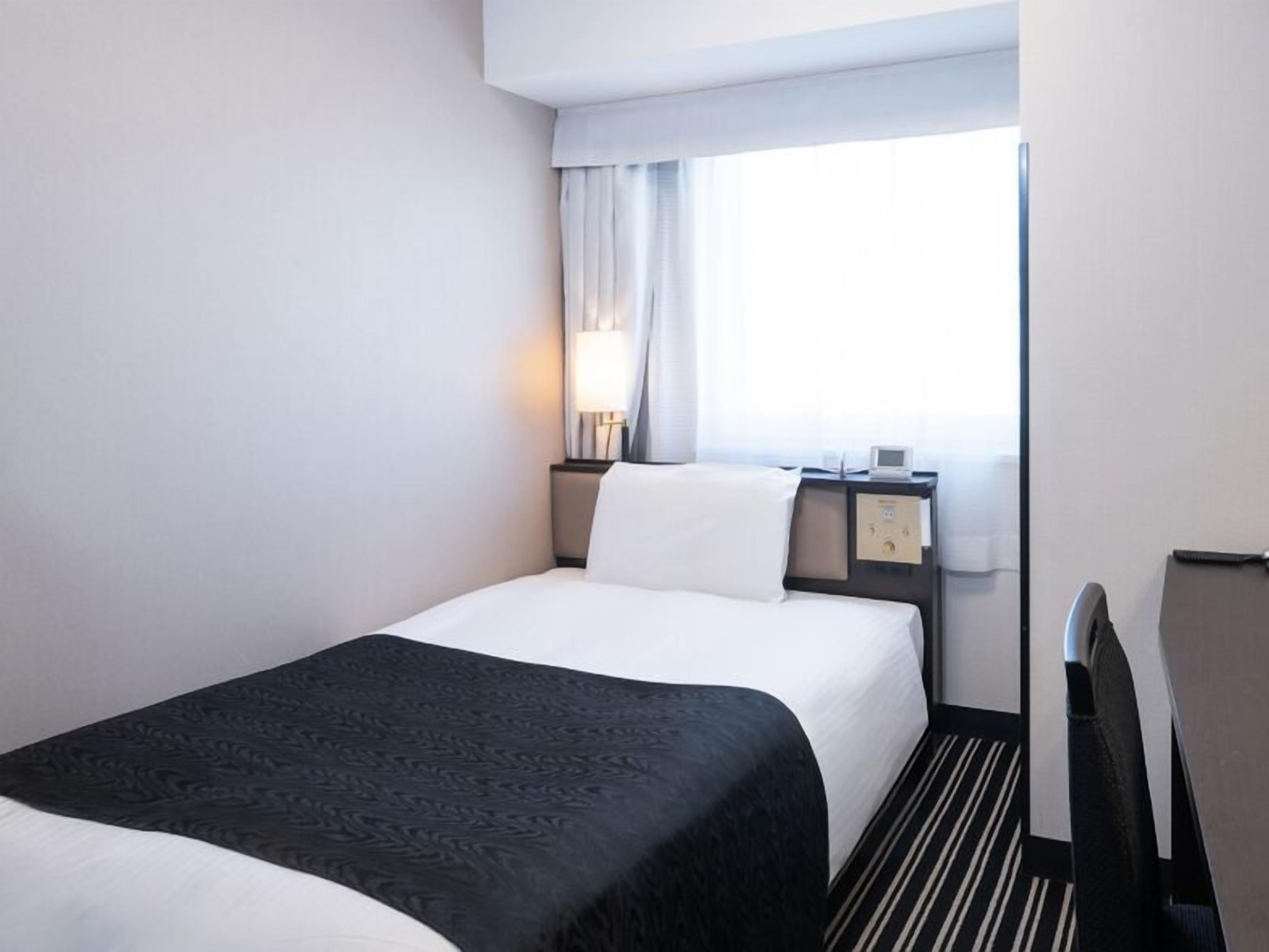 Een hotelkamer met een bed, nachtkastje met lamp, nachtkastje met klok en raam met gordijnen.