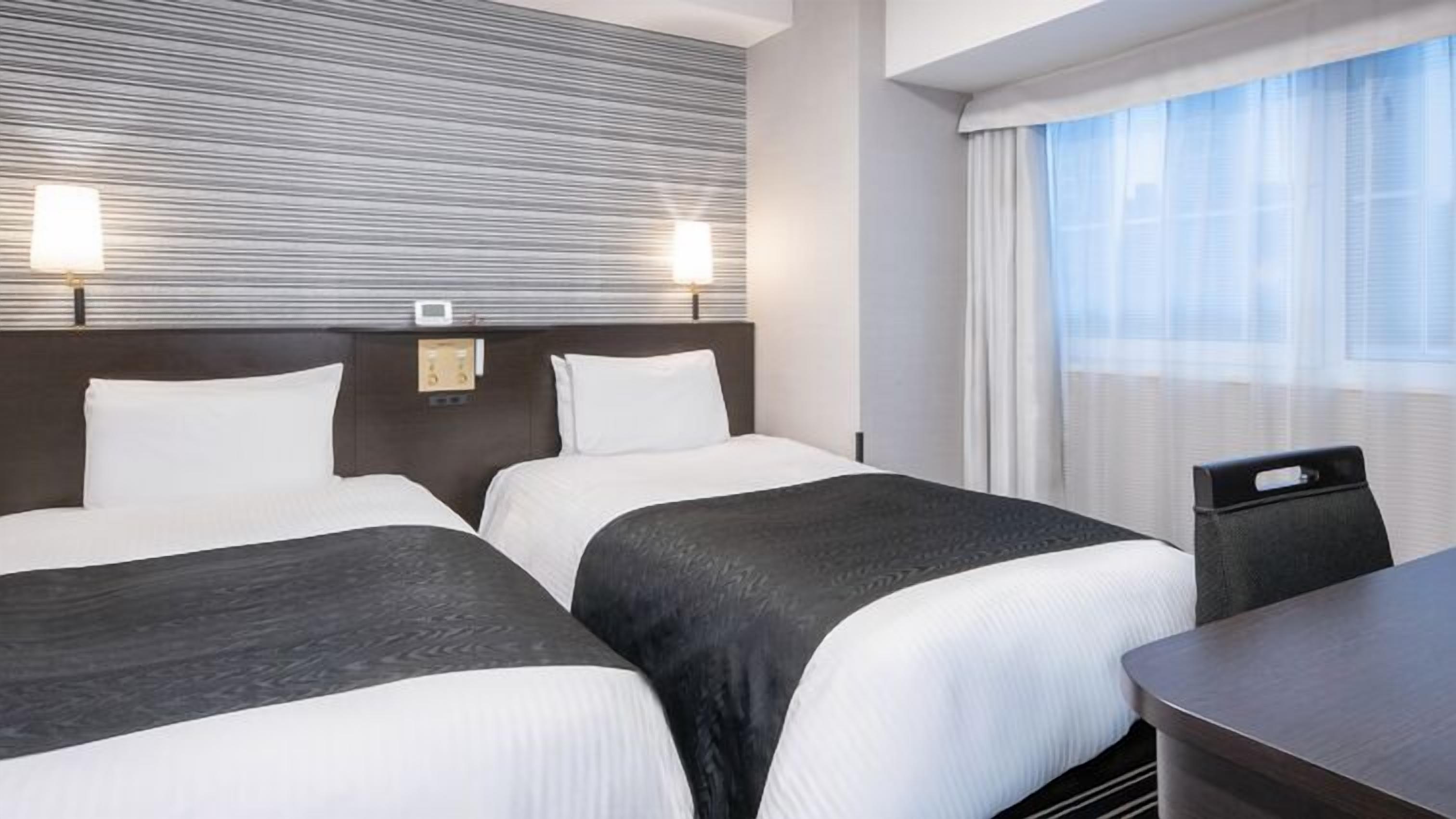 Een hotelkamer met twee bedden, een bureau en een raam met gordijnen.
