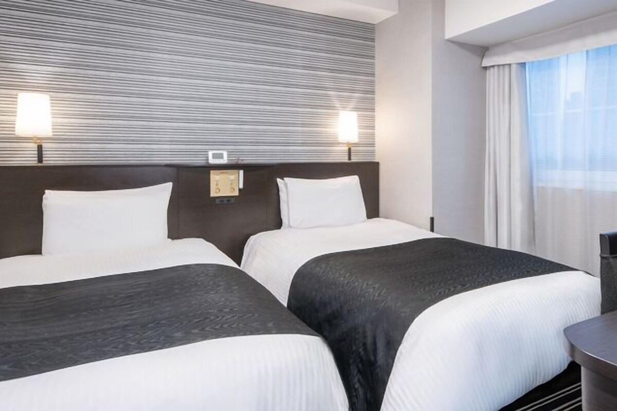 A hotel room with two beds, a desk, and a window with curtains.