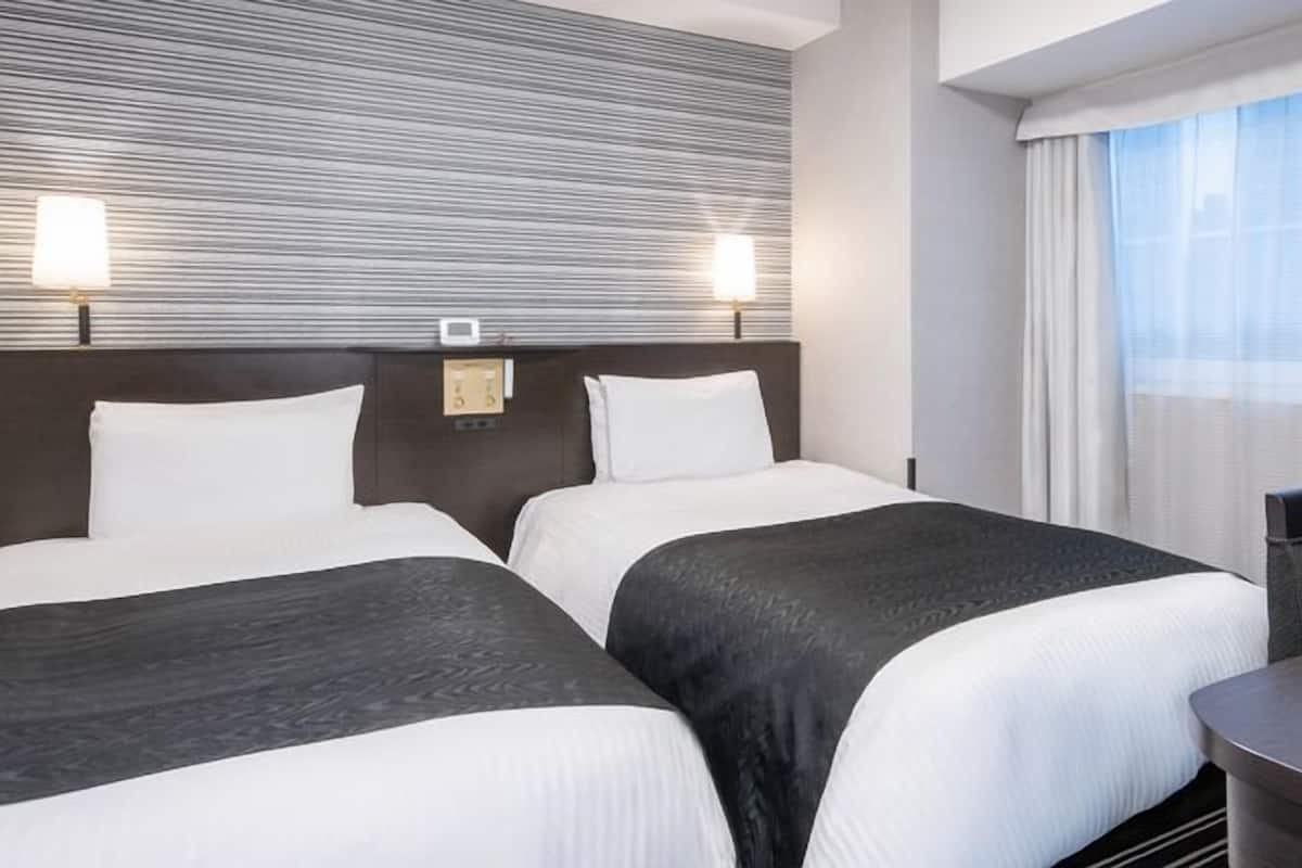 A hotel room with two beds, a desk, and a window with curtains.