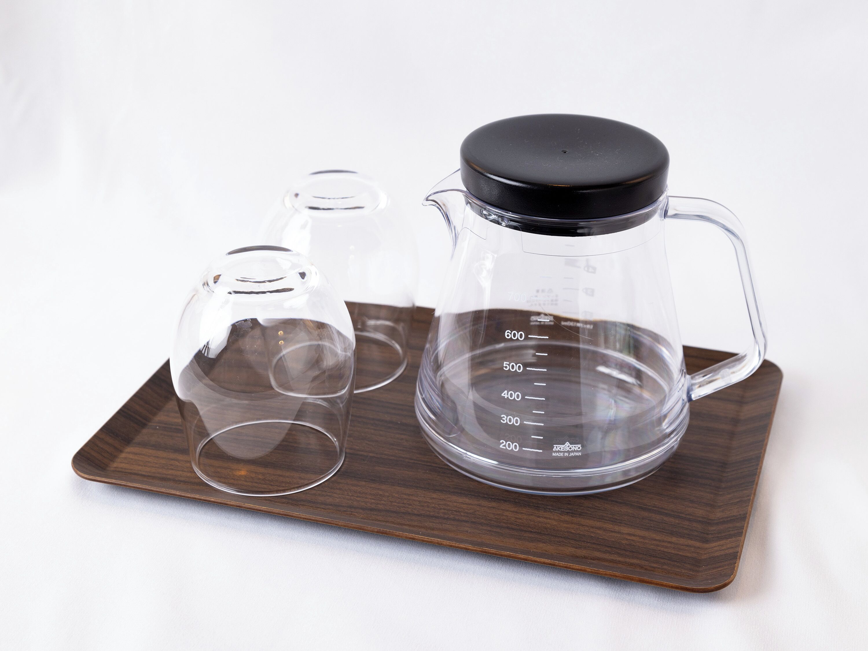 A coffee maker with a measuring cup and two glasses on a wooden tray.