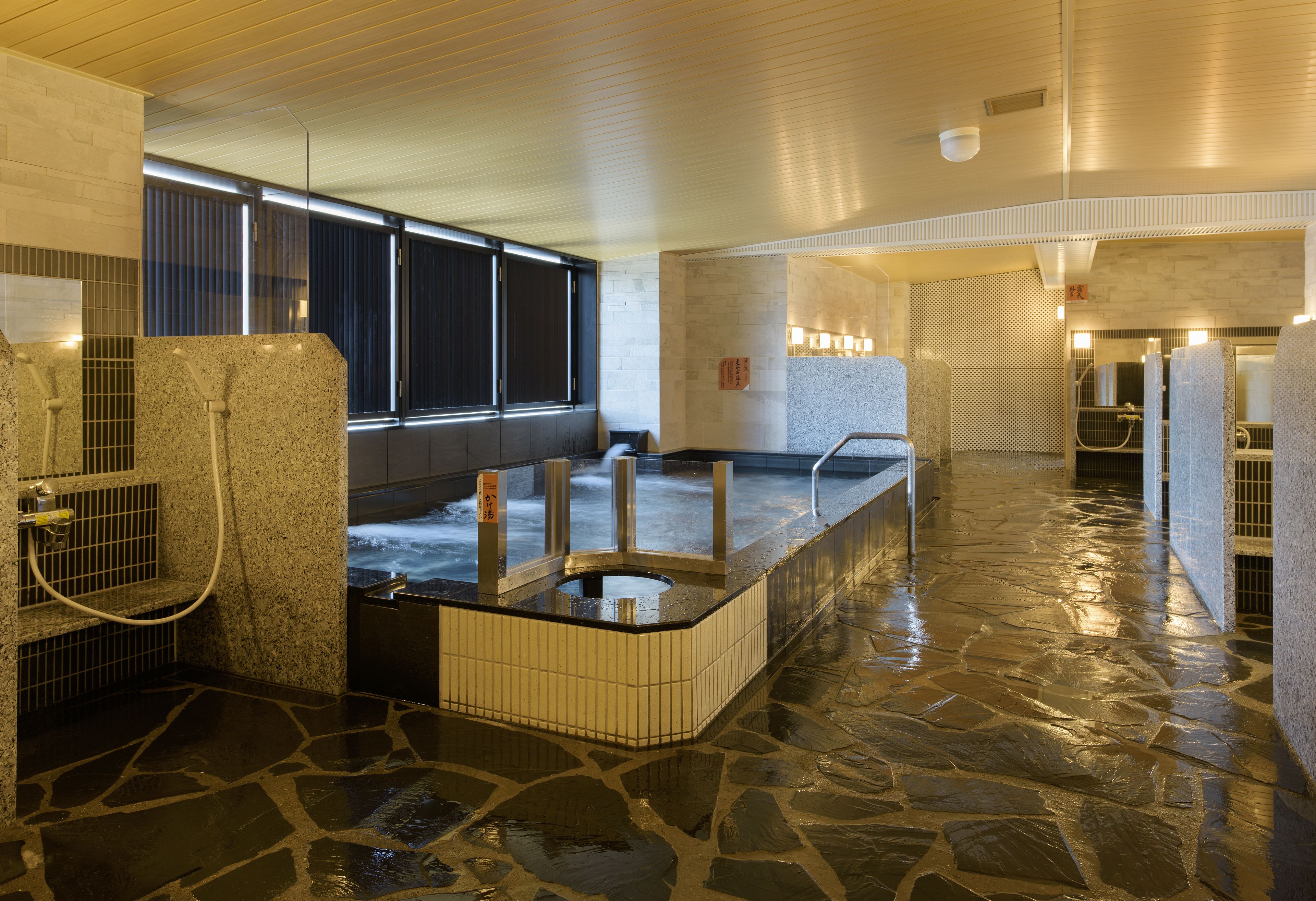 Un spa moderne doté d’un sol en pierre, de plusieurs bains à remous et offrant une vue sur la ville la nuit.