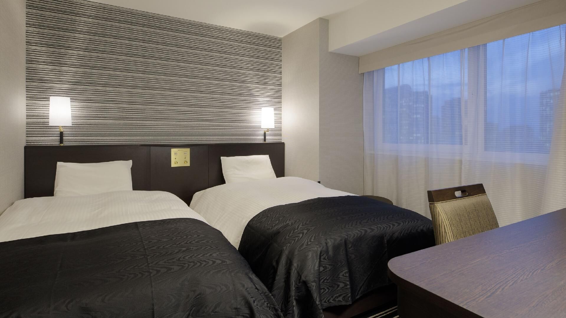 Een hotelkamer met twee bedden, een bureau en een raam met zonwering.
