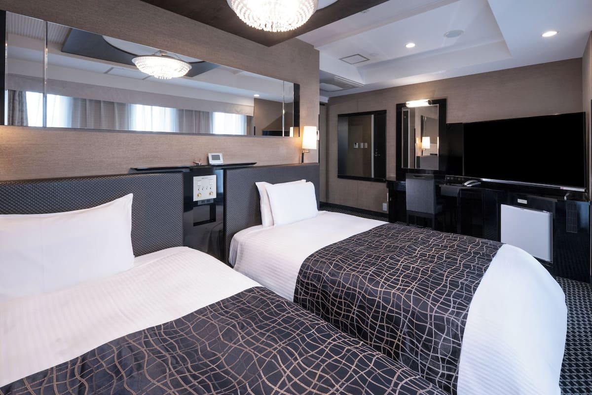Quarto de hotel com duas camas, uma mesa, televisão e minibar.