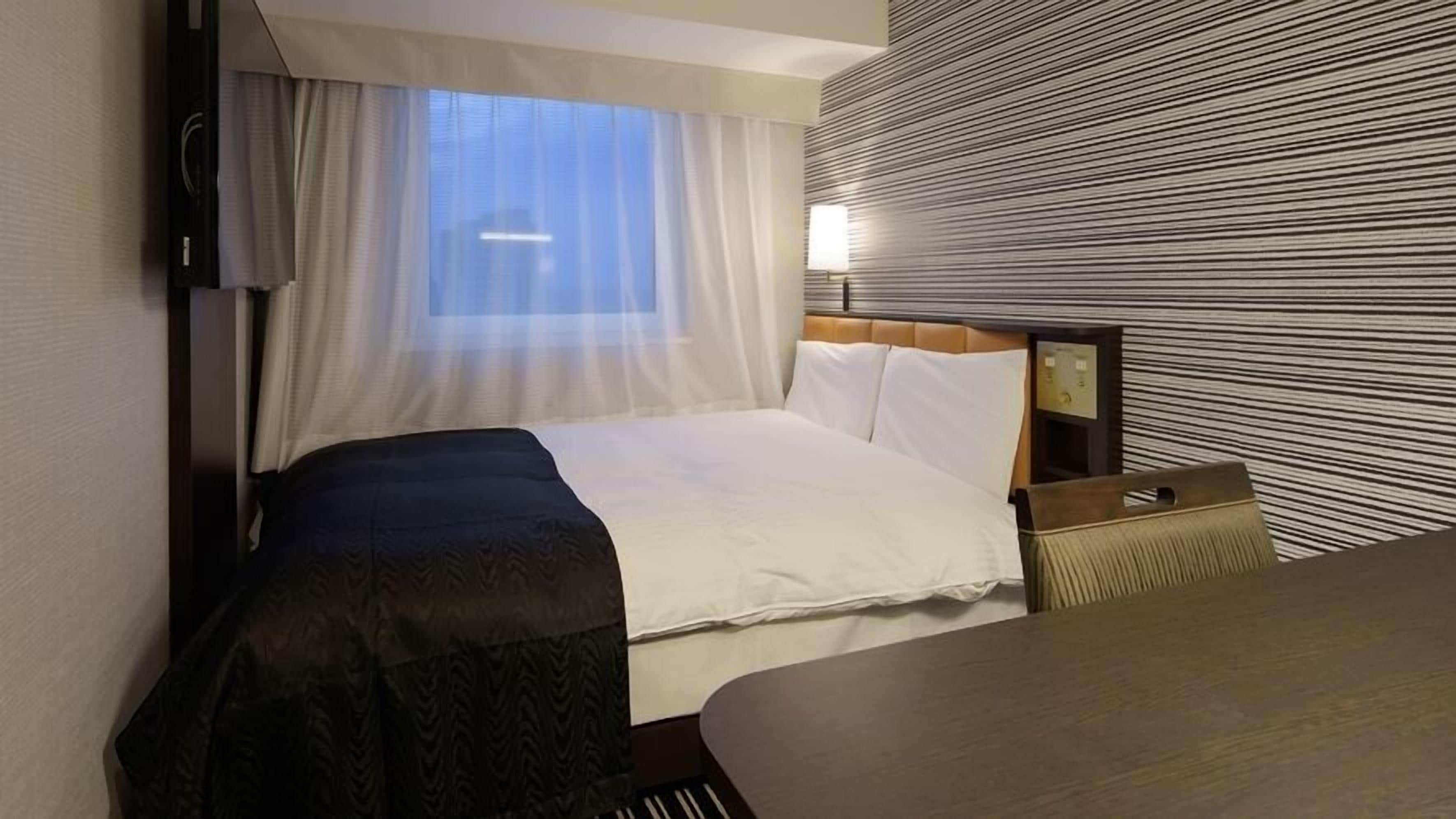 Een hotelkamer met een bed, nachtkastje, lamp en raam met gordijnen.